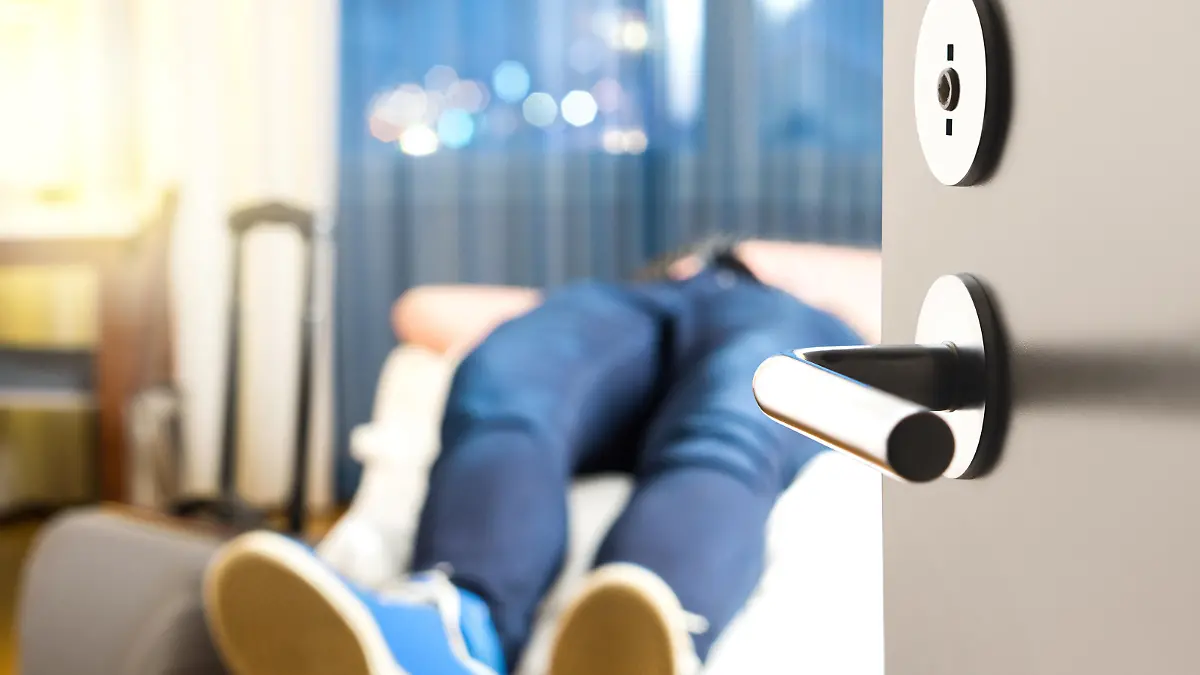 Tired traveler sleeping on hotel room bed. Exhausted man after long flight and travel with baggage. Tourist arrived home from vacation. Lying in bedroom next to suitcase. Sick person after holiday.