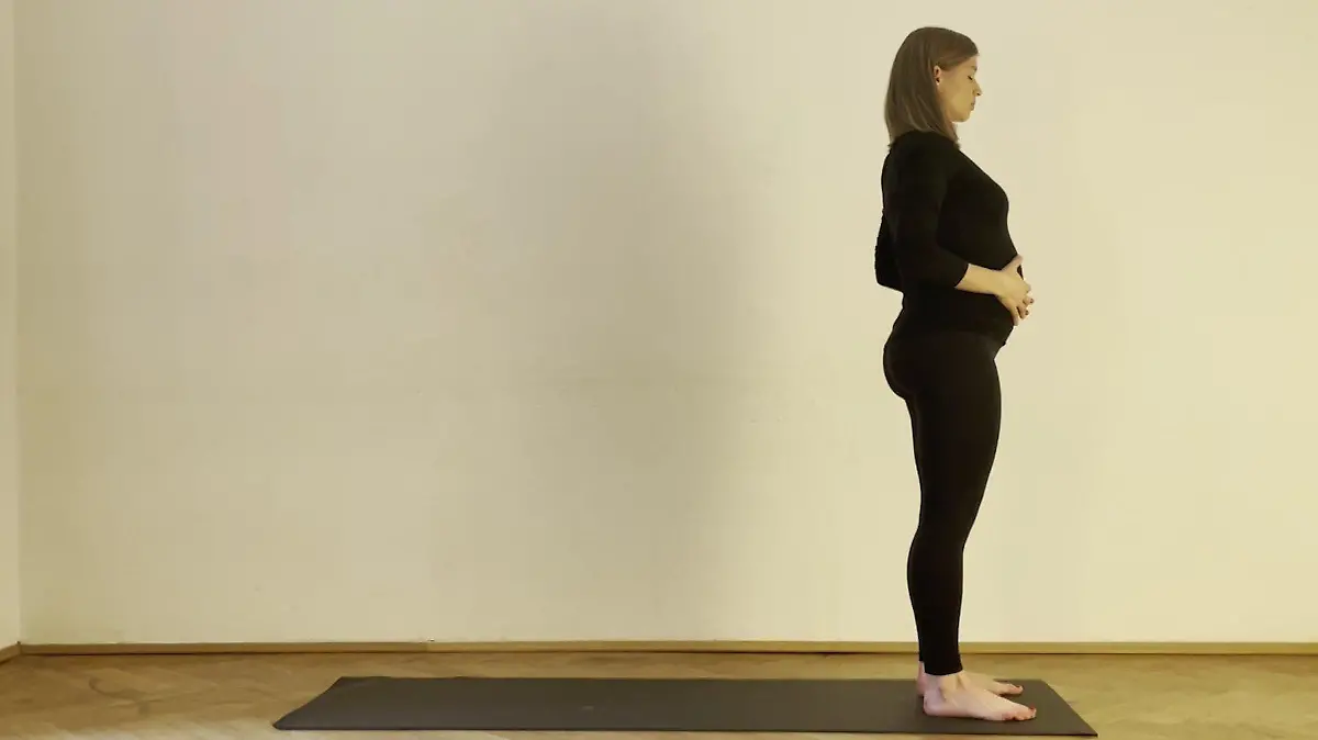 Yoga-Lehrerin Lena Braun steht mit den Händen auf ihrem Bauch am Anfang ihrer Yoga-Matte.