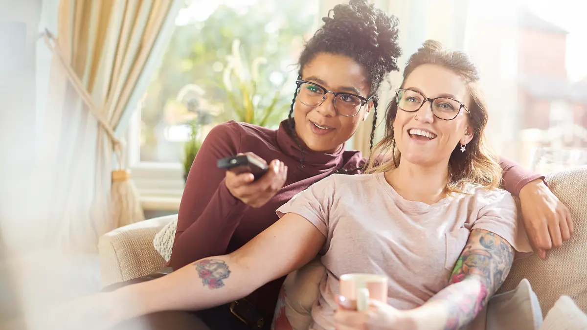 a female same sex couple sit on the sofa watching tv together