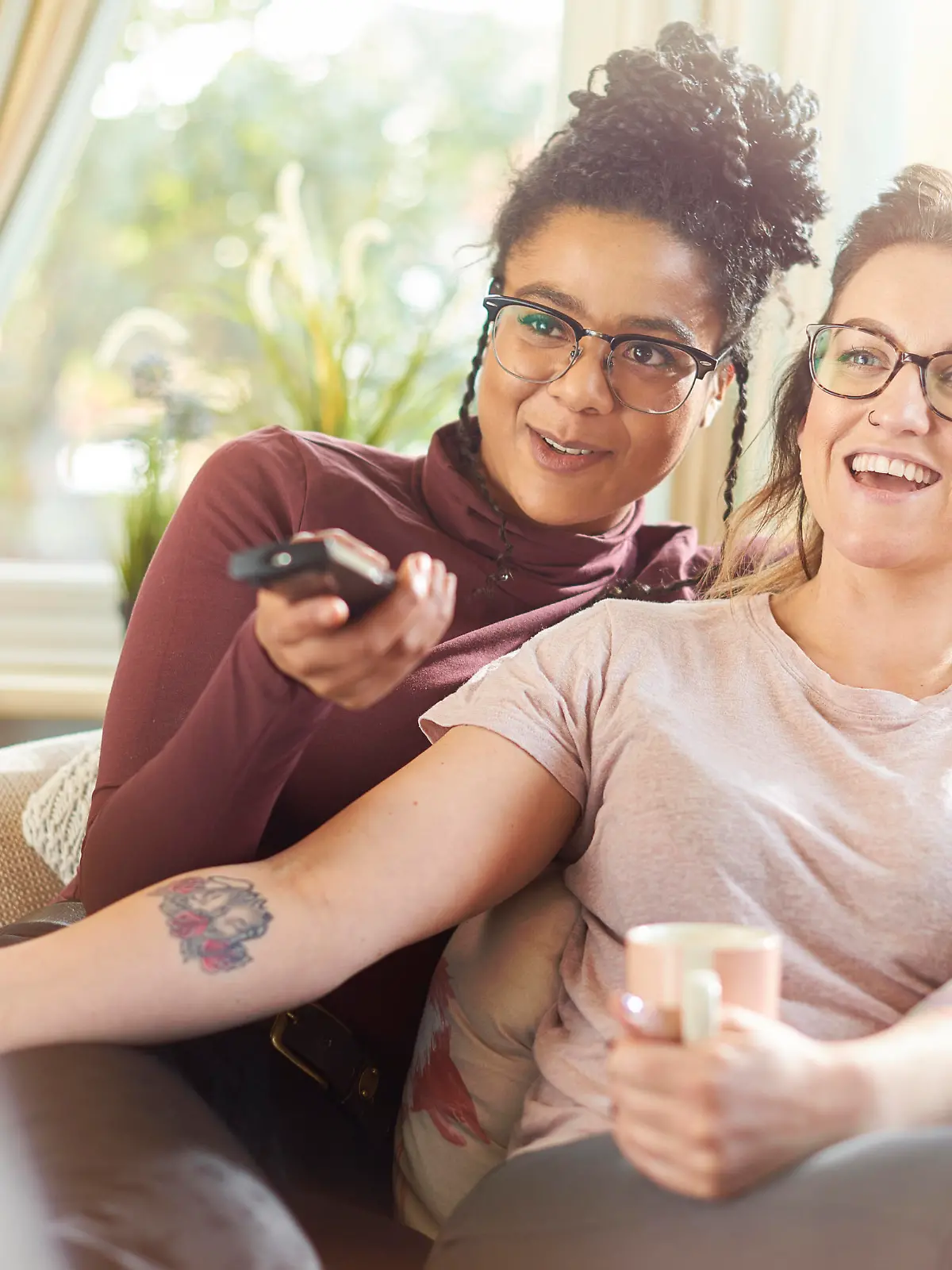 a female same sex couple sit on the sofa watching tv together