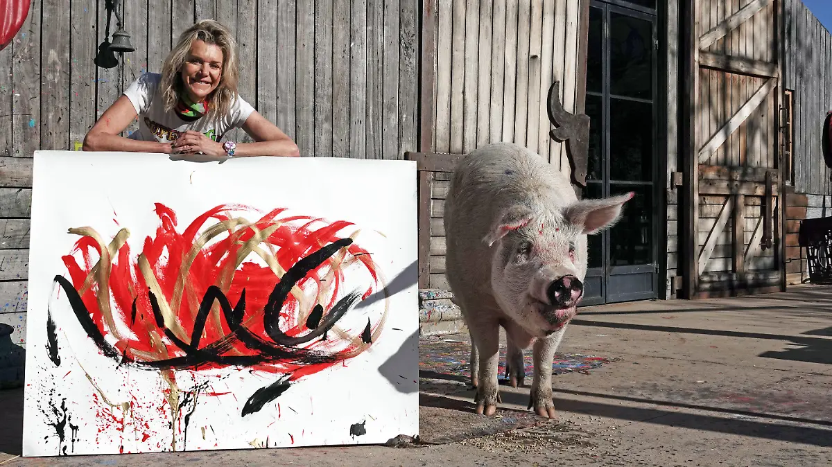 PRODUKTION - 30.05.2022, Südafrika, Franschhoek: Pigcasso, ein malendes Schwein aus Südafrika, steht mit seiner Halterin Joanne Lefson neben einem Bild, das es gemalt hat. (zu dpa-KORR Tierisches Talent: Südafrikanisches Schwein malt saustarke Kunst) Foto: Kristin Palitza/dpa +++ dpa-Bildfunk +++