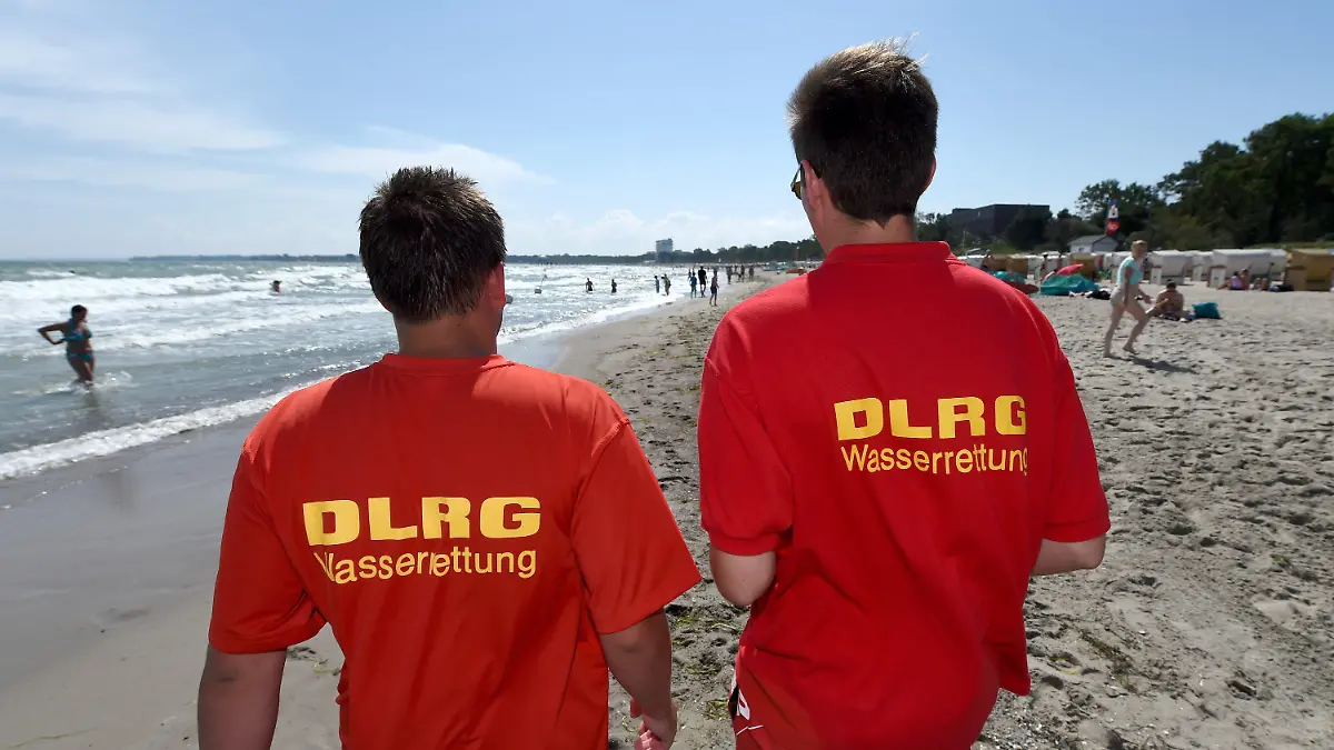 DLRG-Helfer gehen am 22.07.2014 über den Ostseestrand von Timmendorfer Strand (Schleswig-Holstein). Wegen starker Strömung herrscht hier ein Badeverbot. Nach den tödlichen Badeunfällen an der Ostsee hat die Polizei an die Badegäste appelliert, rote Flaggen der DLRG und direkt am Wasser aufgestellte Hinweisschilder zu beachten. Foto: Carsten Rehder/dpa (Zu dpa"Polizei mahnt Badegäste nach Unfällen zur Besonnenheit" vom 22.07.2014) +++(c) dpa - Bildfunk+++