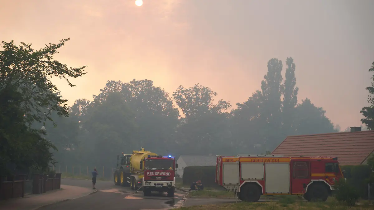 19.06.2022, Brandenburg, Beelitz-Heilstätten: Einsatzfahrzeuge der Feuerwehr werden betankt, während dichter Rauch die Sonne verdeckt. Das Feuer sei außer Kontrolle, womöglich drohe eine Evakuierung von Beelitz, sagte der Bürgermeister. Foto: Joerg Carstensen/dpa +++ dpa-Bildfunk +++
