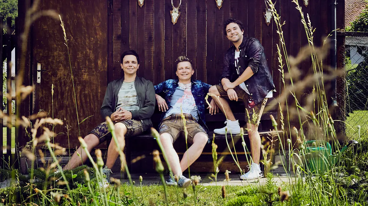 Die Bandmitglieder posieren vor einer braunen Holzwand.