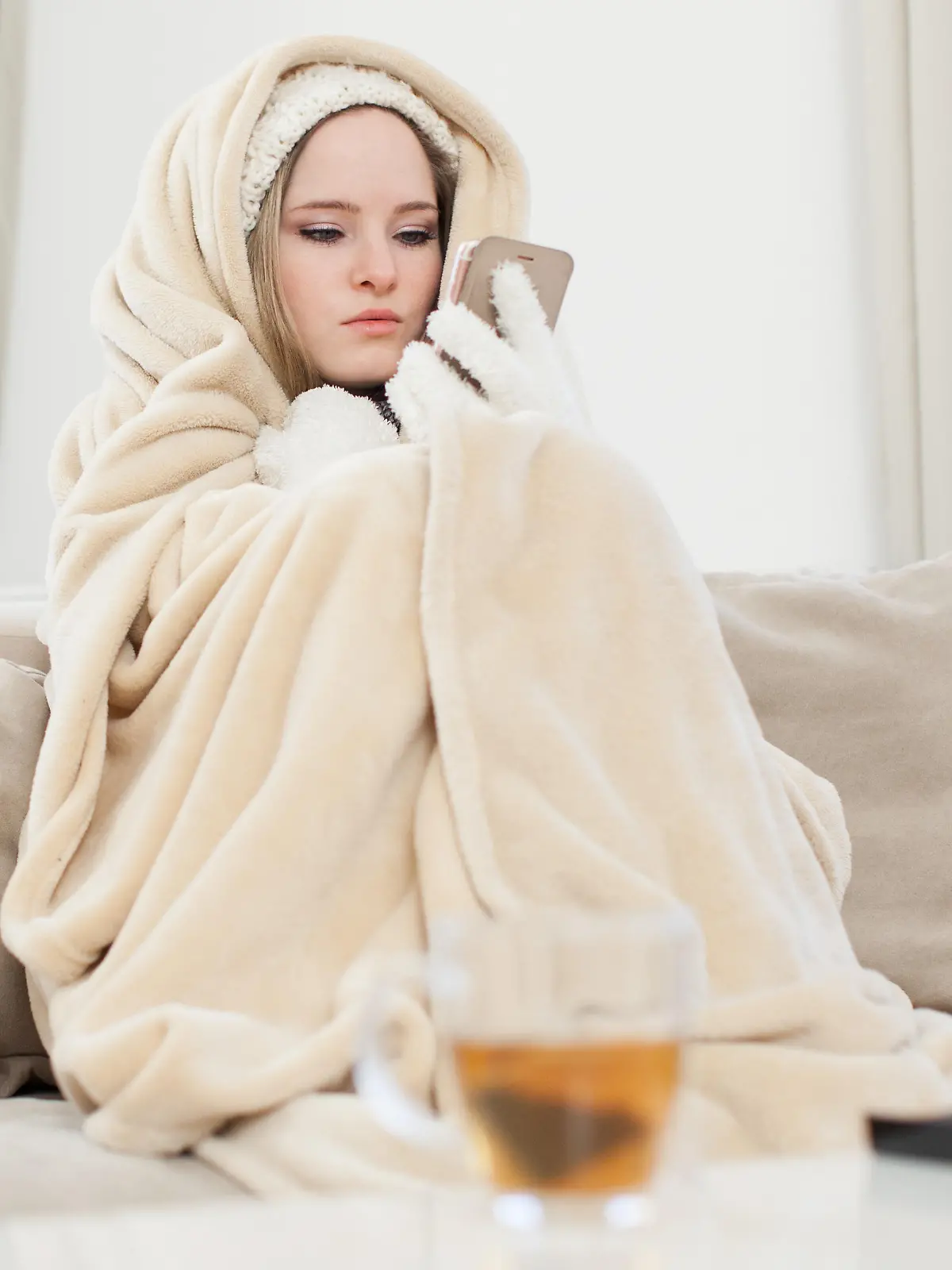 ILLUSTRATION - Eine junge Frau sitzt am 29.11.2016 in einem Wohnzimmer in Hamburg in Decken eingewickelt auf einer Couch und schaut auf ihr Handy, um den Vermieter zu informieren (gestellte Szene). Foto: Christin Klose || Modellfreigabe vorhanden