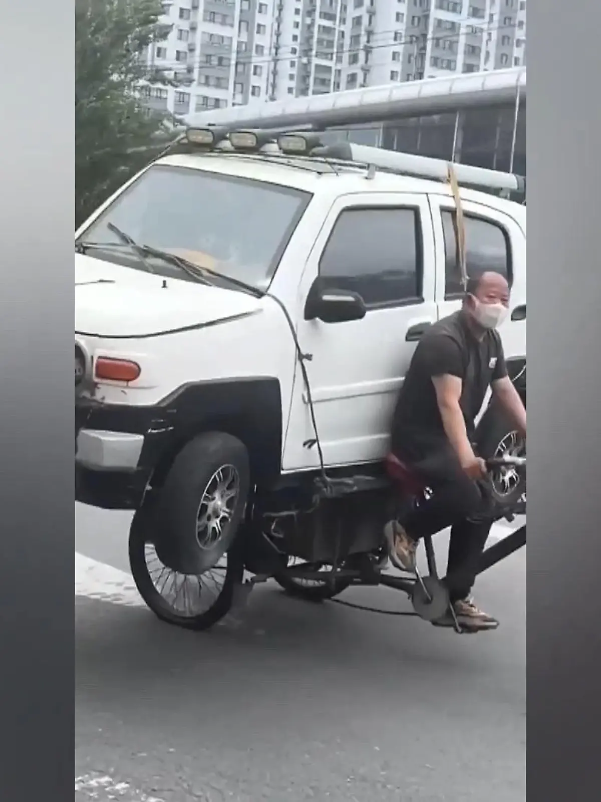 Ein Mann fährt mit einem Dreirad und einem Auto auf dem Gepäckträger über die Straßen einer chinesischen Stadt. Das Auto hat er nur mit ein paar Seilen gesichert. Für ihn scheint es aber das normalste der Welt zu sein. Wenn er das in Deutschland machen würde, würde er nicht sehr weit kommen.