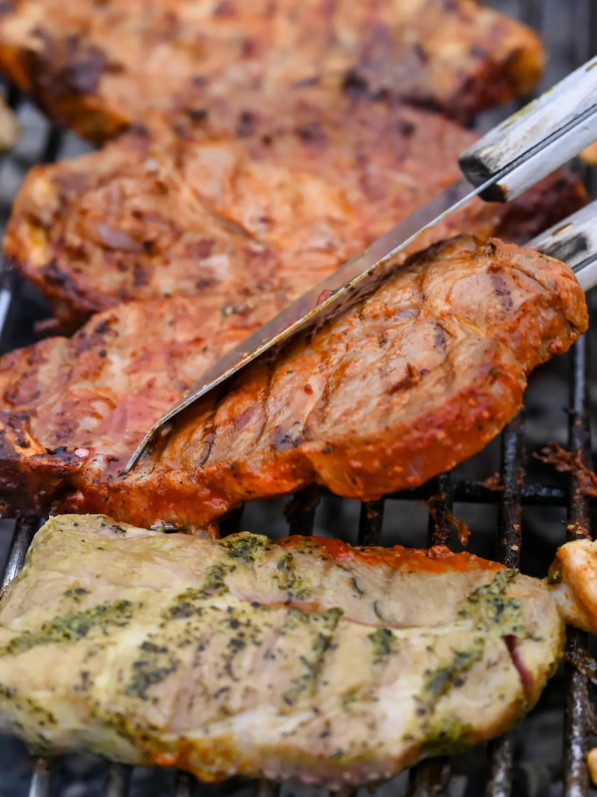 Mehrere Stücken mariniertes Schweinefleisch und Hühnerfleisch liegen auf einem Holzkohlegrill.