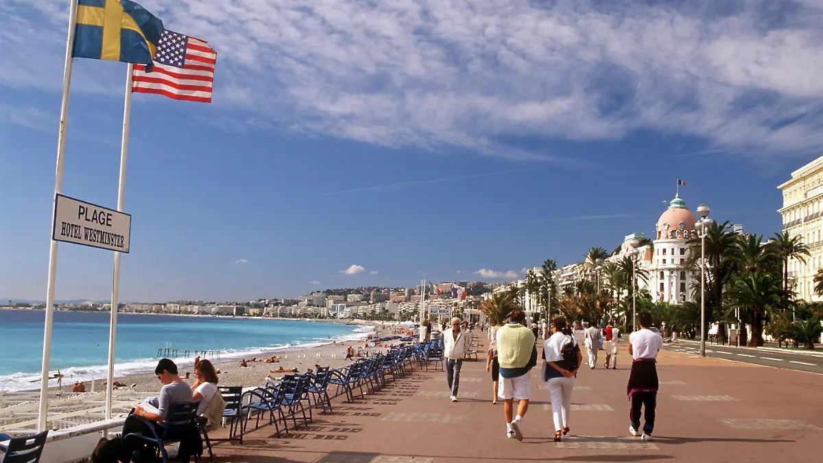 Passanten flanieren auf der Promenade des Anglais in Nizza an der französischen Riviera. Im Hintergrund rechts das Hotel Negresco. (Aufnahme von 2001).