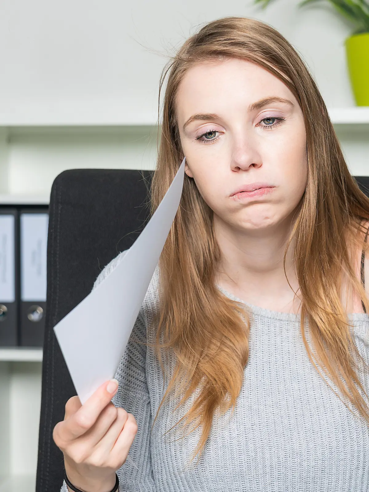 A woman in the office is waving her head with a sheet of paper