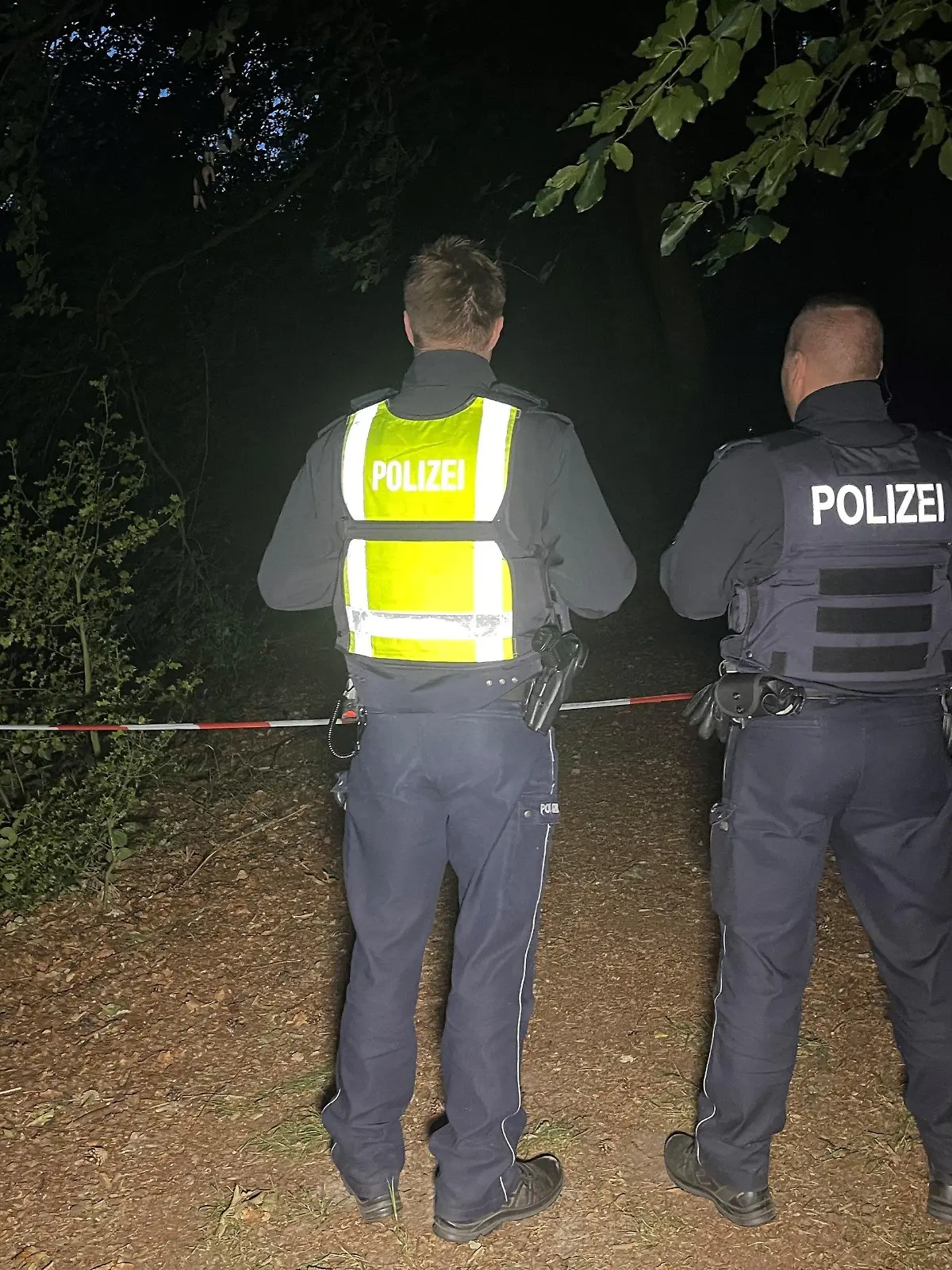 16.07.2023, Nordrhein-Westfalen, Halle: Polizisten stehen an einem abgesperrten Waldstück zwischen Halle-Kölkebeck undd Hesselteich, einem Ortsteil von Versmold.  Spaziergänger hatten in dem Waldstück im Kreis Gütersloh eine Leiche gefunden. Die weiteren Ermittlungen zur Feststellung der Identität sowie der Todesursache übernahm eine Mordkommission des Polizeipräsidiums Bielefeld. Foto: Christian Müller/Westfalennews/dpa +++ dpa-Bildfunk +++