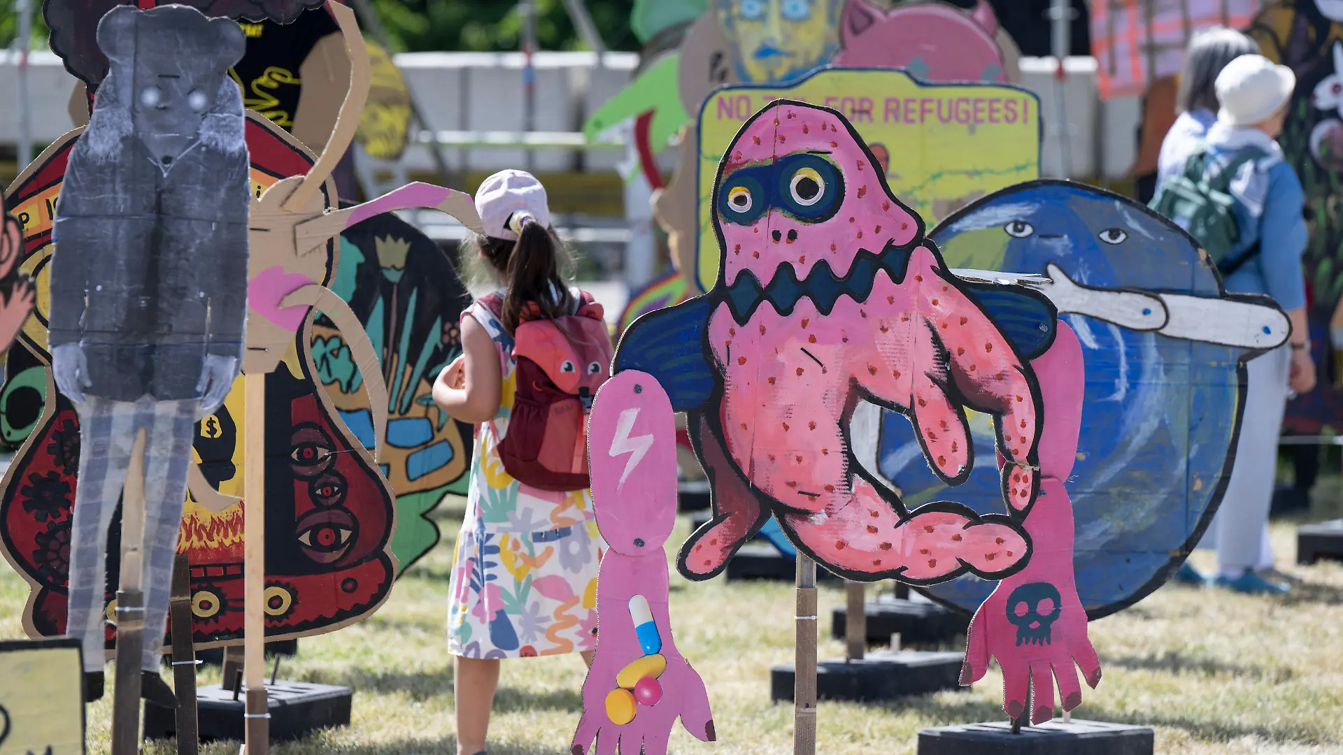 17.06.2022, Hessen, Kassel: Besucher gehen zwischen riesigen Pappfiguren der indonesischen Künstlergruppe ·Taring Padi· auf dem Friedrichsplatz hindurch. Die internationale Kunstausstellung documenta fifteen ist zunächst für Fachbesucher geöffnet, ab dem 18. Juni 2022 steht sie allen Interessierten offen. Foto: Boris Roessler/dpa - ACHTUNG: Nur zur redaktionellen Verwendung im Zusammenhang mit einer Berichterstattung über die documenta 15 und nur mit vollständiger Nennung des vorstehenden Credits +++ dpa-Bildfunk +++