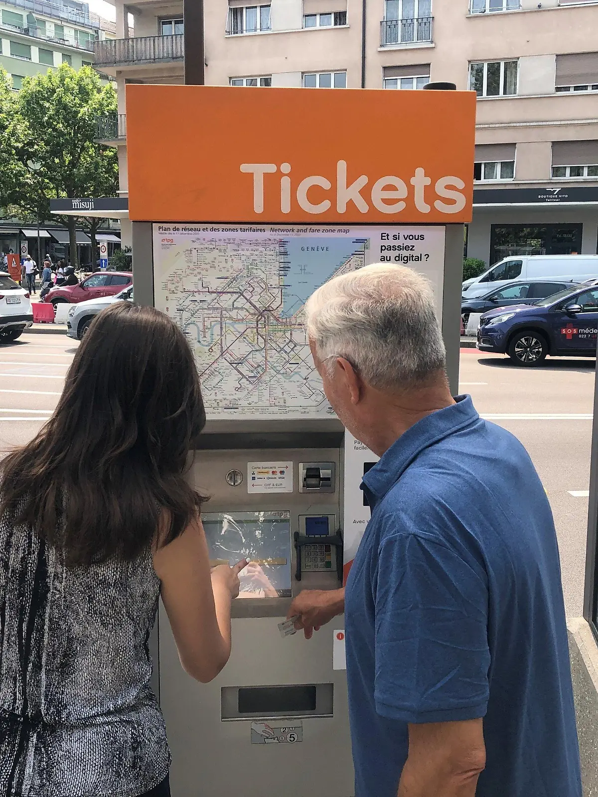 PRODUKTION - 29.06.2023, Schweiz, Genf: Sama Mamadova und Karim Hamza versuchen an einem Ticket-Automaten eine Fahrkarte zu erwerben. Das Phänomen kennt jeder: Man steht vor einem Fahrkartenautomaten und eine simple Fahrkarte zu erstehen ist kompliziert. Mit der Nervosität steigt der Frust und die Fluch-Lautstärke. (zu dpa «Monster Fahrkartenautomat: warum Ticketkaufen oft kompliziert ist») Foto: Christiane Oelrich/dpa +++ dpa-Bildfunk +++
