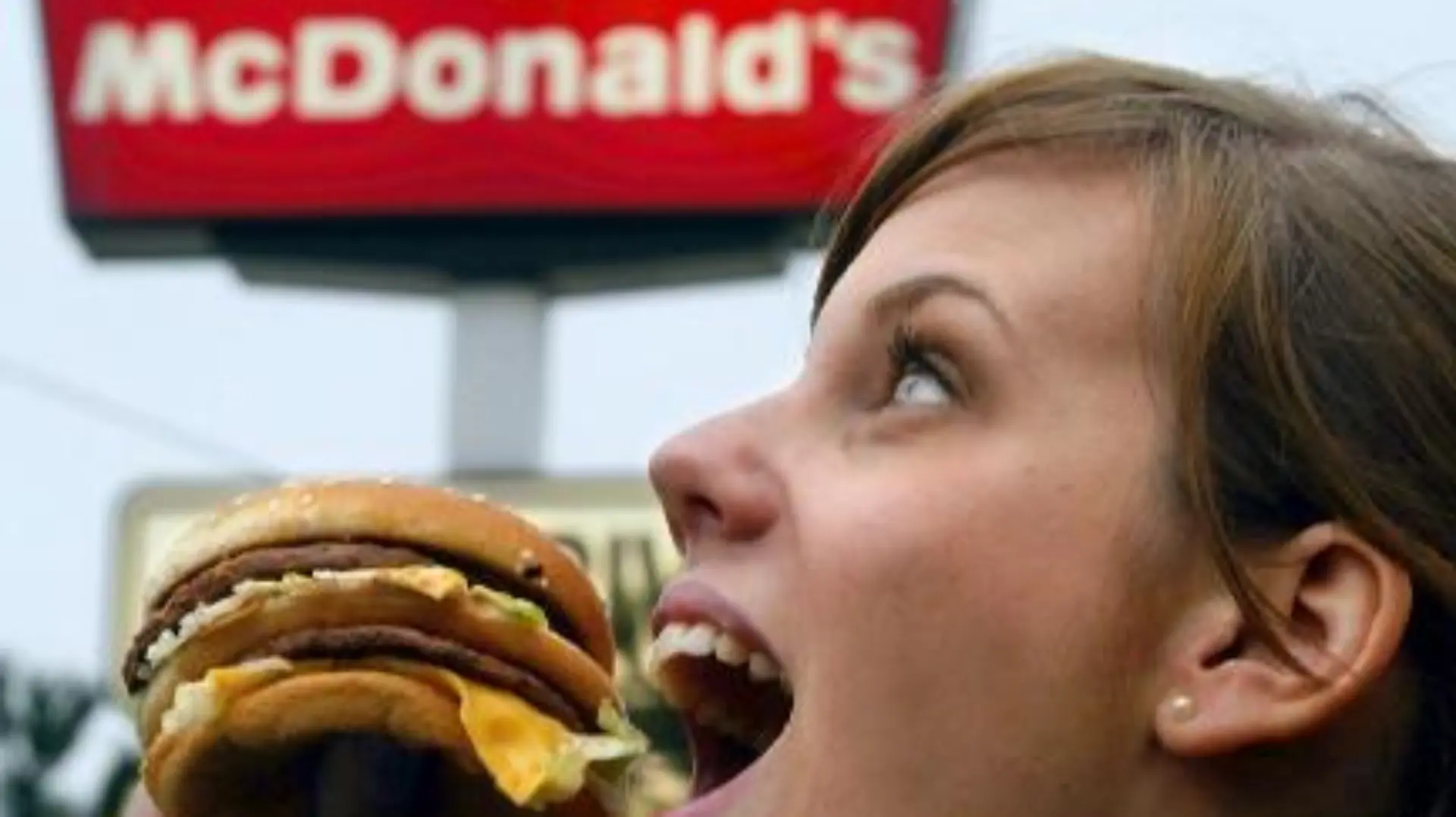 Eine junge Frau isst am 23.1.2003 vor einer Leuchtreklame eines McDonald's-Restaurants in Düsseldorf einen Hamburger.