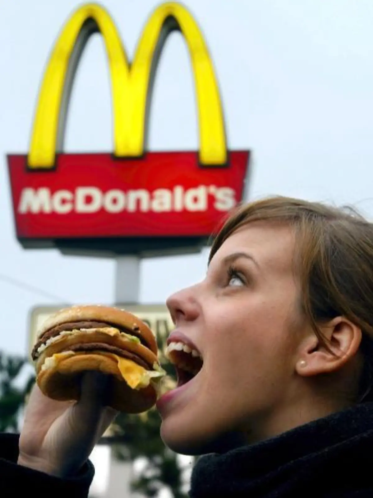 Eine junge Frau isst am 23.1.2003 vor einer Leuchtreklame eines McDonald's-Restaurants in Düsseldorf einen Hamburger.