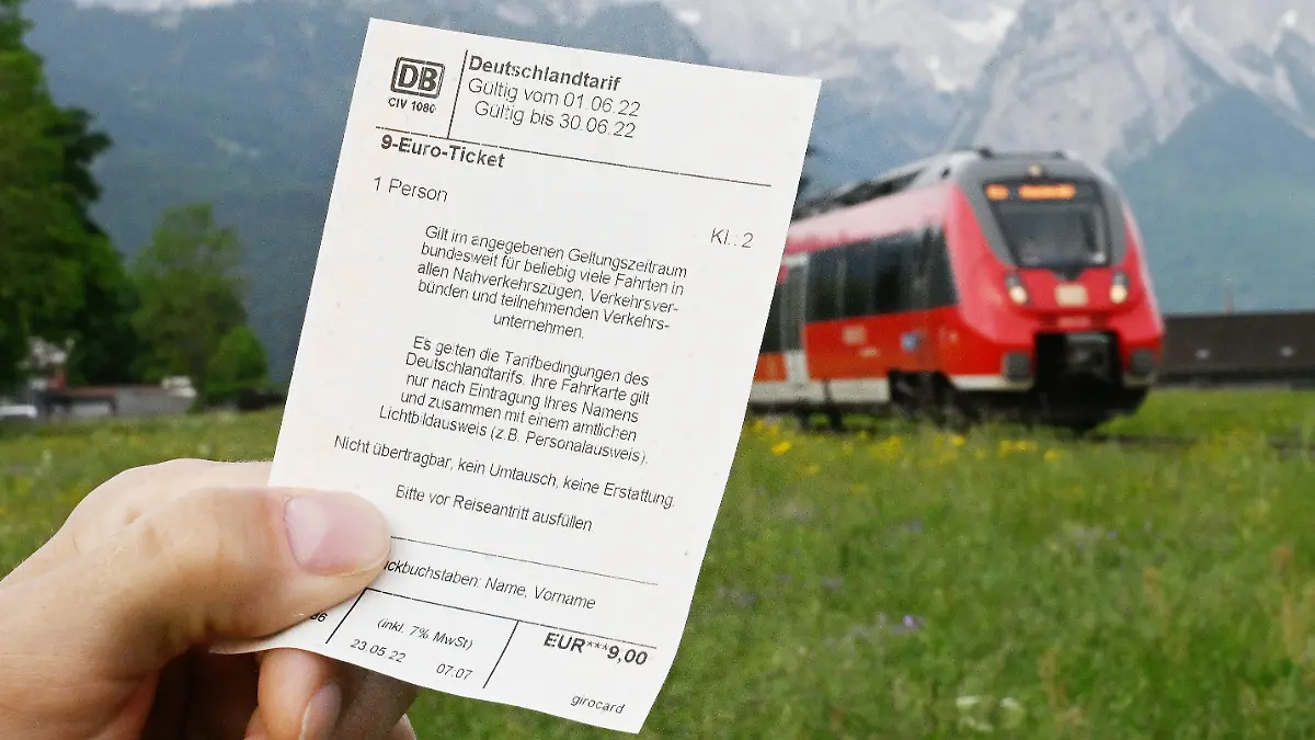 ARCHIV - 23.05.2022, Bayern, Garmisch-Partenkirchen: Ein Mann hält ein 9-Euro-Ticket in der Hand, im Hintergrund fährt ein Zug der Deutschen Bahn vor der Bergkulisse des Wettersteingebirges vorbei (gestelltes Foto). In Zügen auf dem Weg in die Alpen könnte es am langen Wochenende in Bayern wegen des günstigen Angebots voller werden. (zu dpa: «Ausflugsorte erwarten an Pfingsten wegen 9-Euro-Ticket mehr Andrang») Foto: Angelika Warmuth/dpa +++ dpa-Bildfunk +++