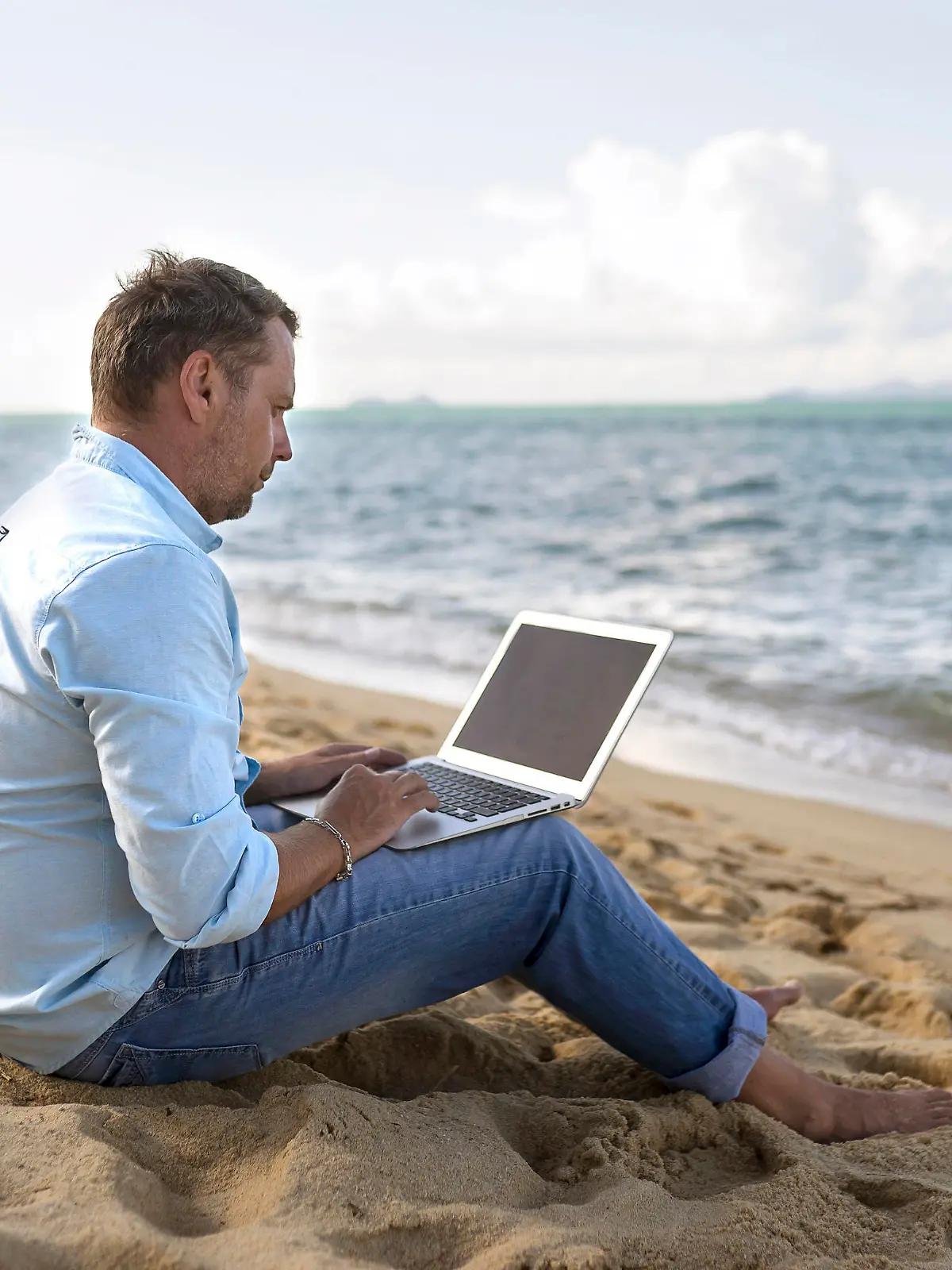 Caucasian man sitting on beach using laptop, Kaukasischer Mann sitzt am Strand mit Laptop || Modellfreigabe vorhanden
