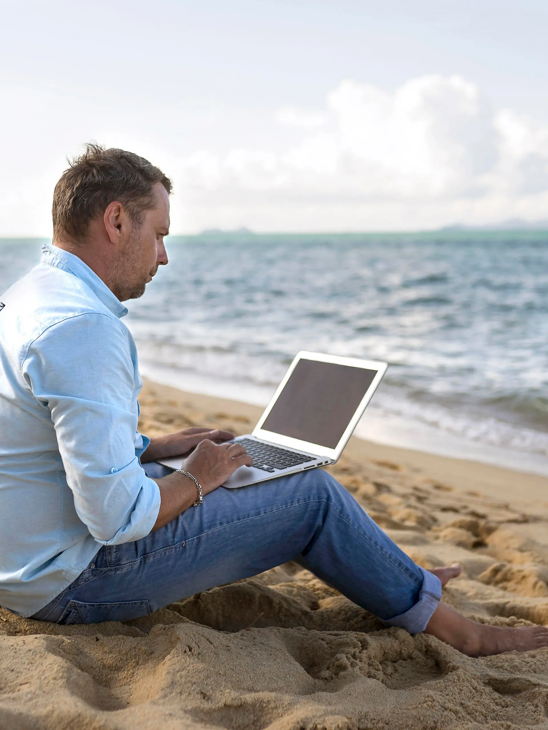Caucasian man sitting on beach using laptop, Kaukasischer Mann sitzt am Strand mit Laptop || Modellfreigabe vorhanden
