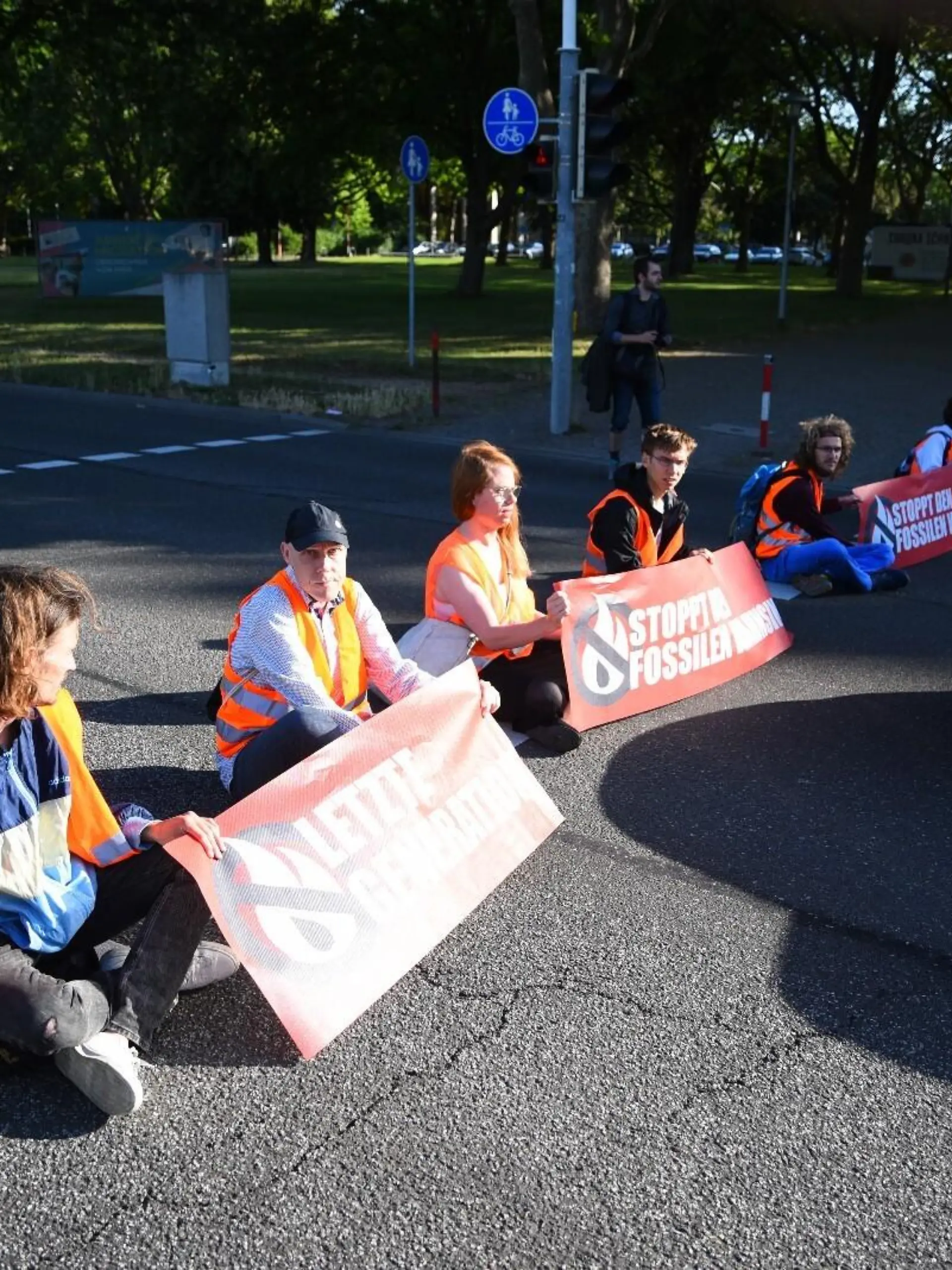 Aktivisten der Gruppe «Letzte Generation» sitzen bei einer Blockade auf einer Straße. Auf einem Spruchband steht: "Stoppt den fossilen Wahnsinn".