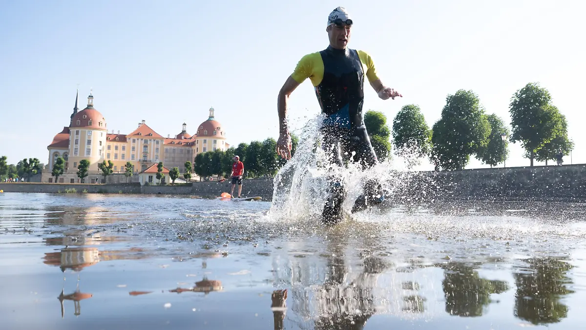 Ein Teilnehmer des Moritzburger Schloss-Triathlon läuft vor der Kulisse des Schloss Moritzburg aus dem Schlossteich. Nach zwei Jahren coronabedingter Absagen feiert der Triathlon das 20. Jubiläum.