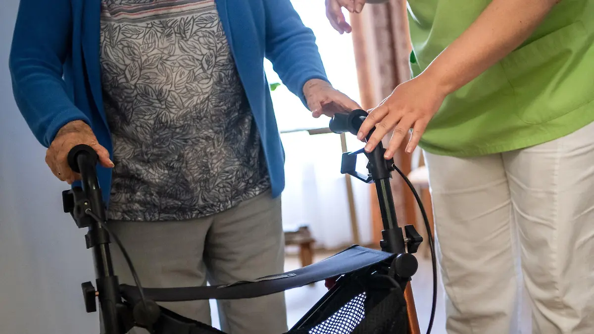 ARCHIV - 16.06.2021, Niedersachsen, Nienburg: Eine Pflegefachkraft hilft einer Bewohnerin in einem Seniorenheim mit ihrem Rollator. Für Bewohnerinnen und Bewohner in Pflegeheimen sind selbst zu zahlende Anteile noch weiter gestiegen.(zu dpa "Zuzahlungen für Pflege im Heim noch weiter gestiegen ") Foto: Sina Schuldt/dpa +++ dpa-Bildfunk +++