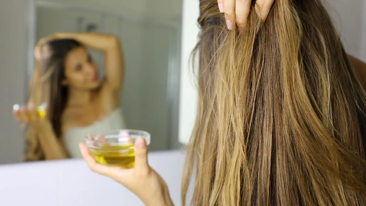 Young woman applying olive oil mask on hair in front of a mirror. Hair care concept. Focus on hair.