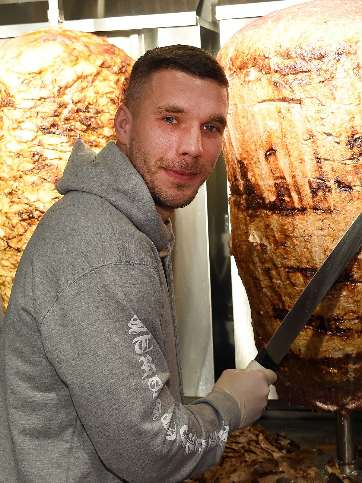 dpatopbilder - Fußball-Weltmeister Lukas Podolski steht am 06.01.2018 in Köln (Nordrhein-Westfalen) bei der Eröffnung eines Döner-Ladens an einem Dönerspieß. Podolski ist Mitgesellschafter bei «Mangal Döner» Foto: Henning Kaiser/dpa +++(c) dpa - Bildfunk+++