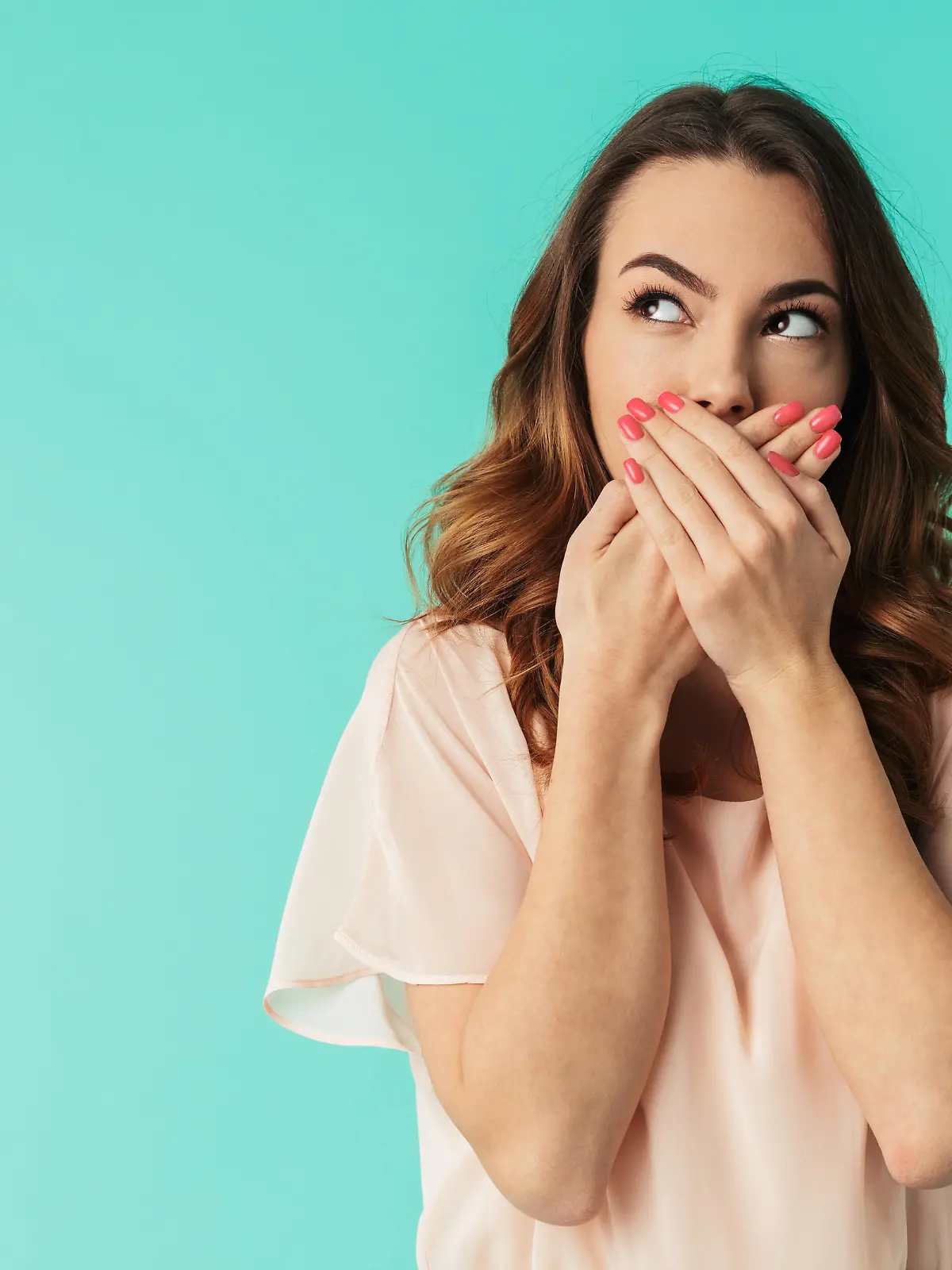 Portrait of a lovely young girl in dress standing with mouth covered and looking away at copy space isolated over blue background