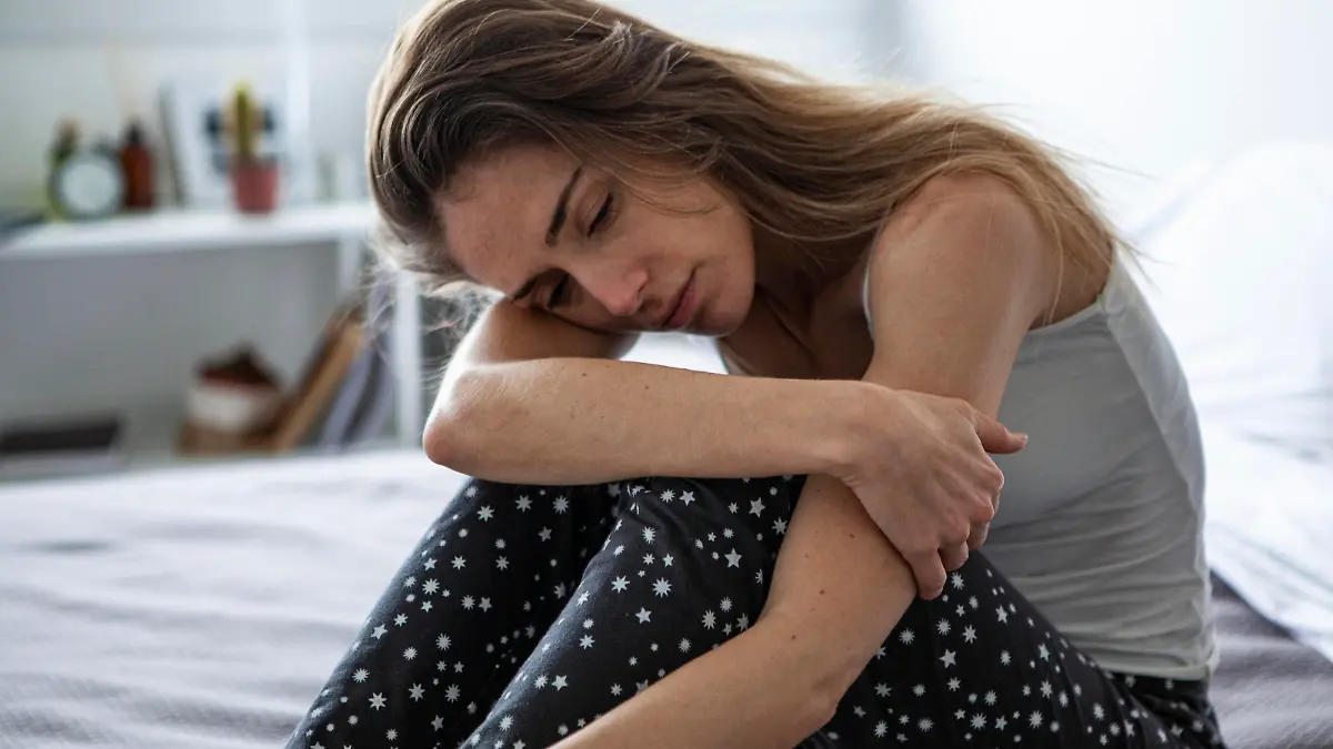 Sad woman looking away while sitting on bed in bedroom