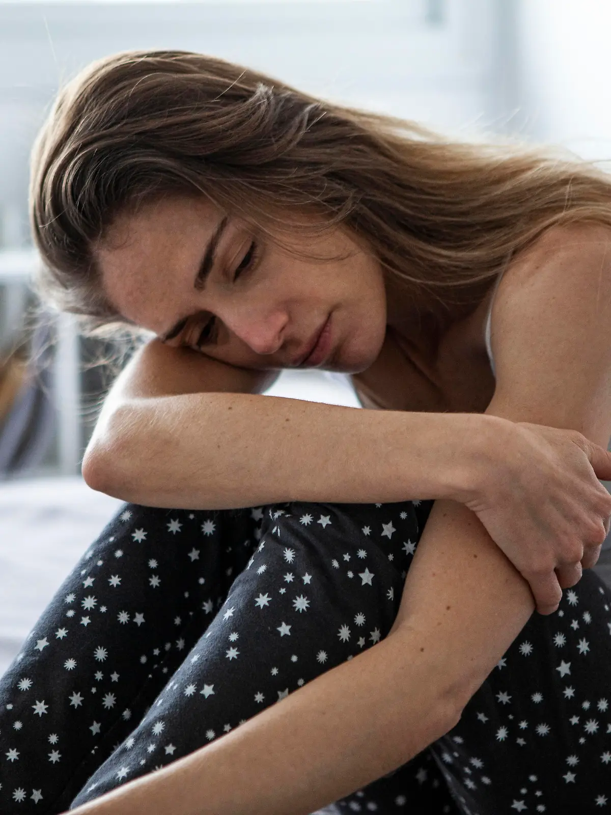 Sad woman looking away while sitting on bed in bedroom