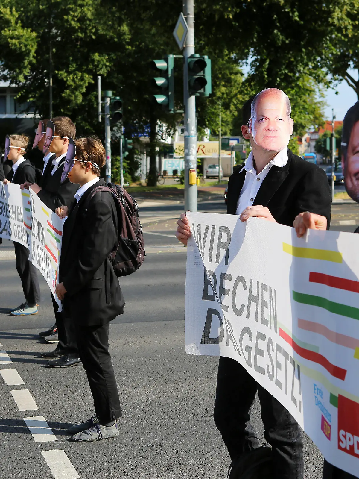 14.07.2023, Niedersachsen, Göttingen: Klimaaktivisten der Gruppe Letzte Generation stehen mit Masken von Bundeskanzler Scholz (2.v.r) und Wirtschaftsminister Habeck (r) bei einer Blockade auf einer Straßenkreuzung. Die Aktivisten halten ein Banner mit der Aufschrift «Wir brechen das Gesetz!». Foto: Stefan Rampfel/dpa +++ dpa-Bildfunk +++