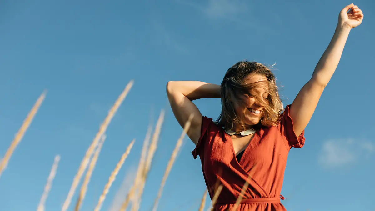 Summer freedom and relaxing leisure. Young happy woman raising arms to feel the breeze at the beach.