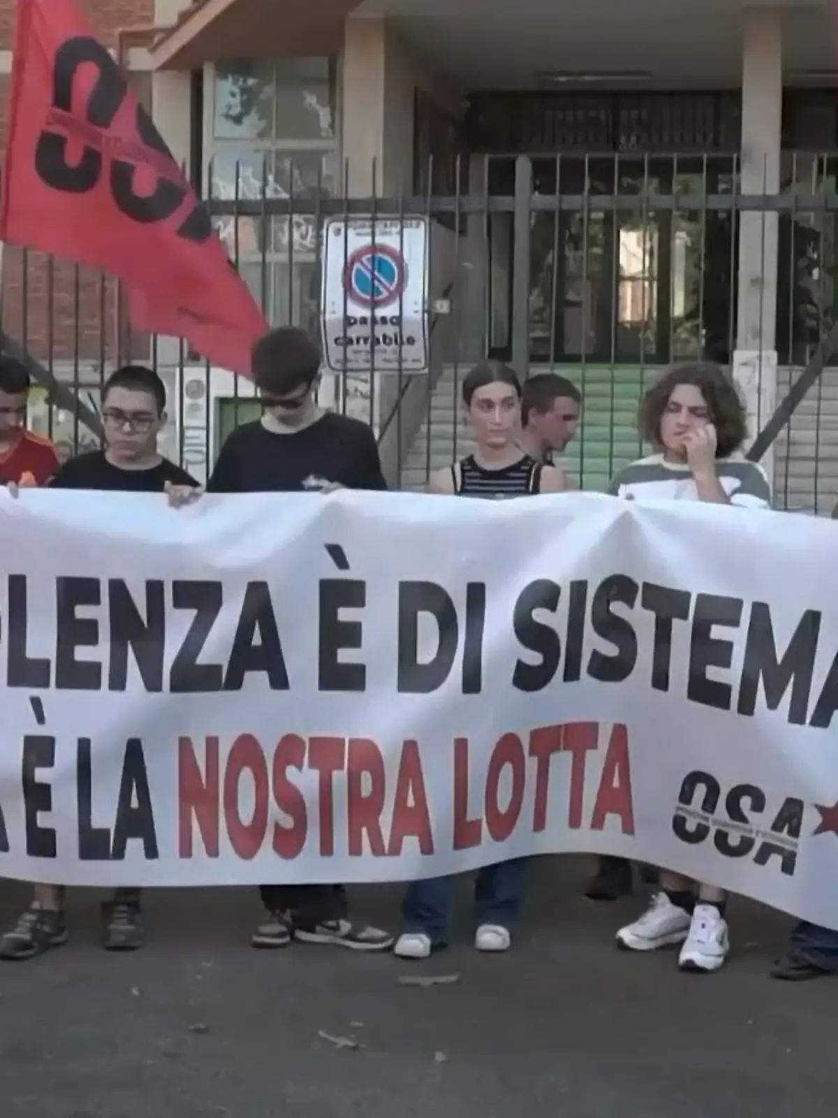 Demonstranten stehen vor einem Gebäude und halten ein Transparent und Fahnen.