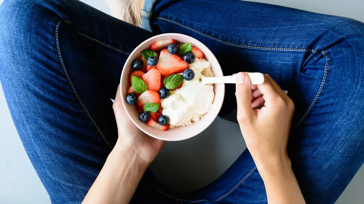 Woman hands holding bowl with cottage cheese, cream, strawberry, blueberry and mint leaves on gray background. Top view. Healthy lifestyle