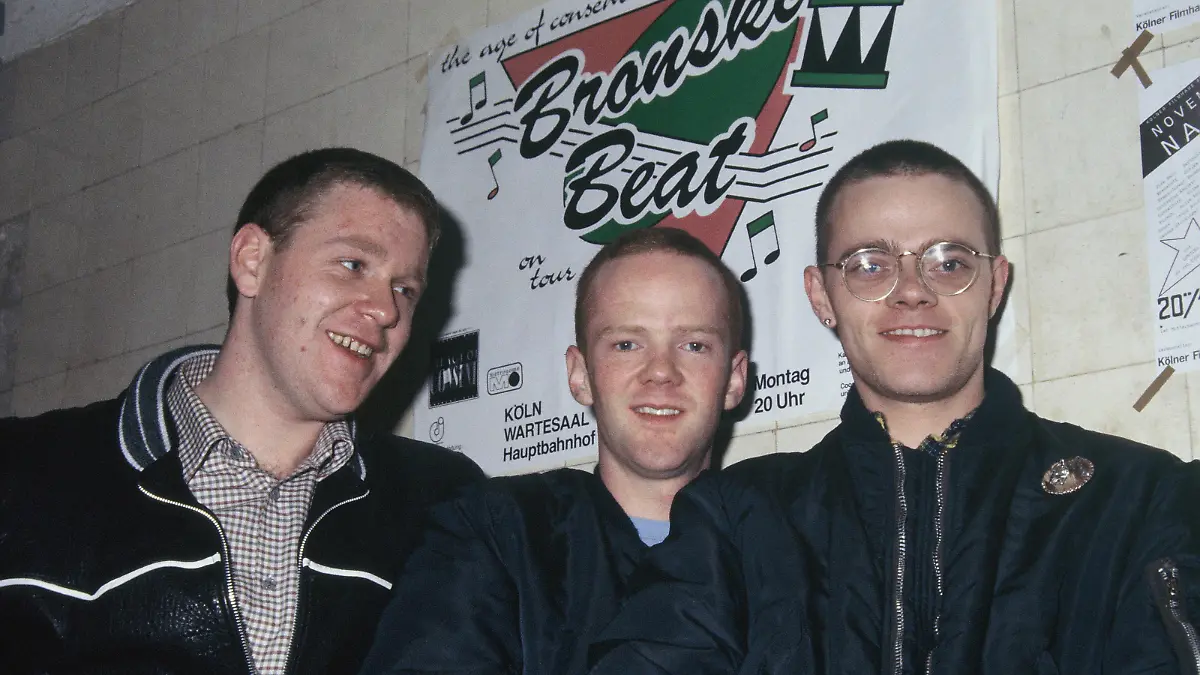 Die britische Band Bronski Beat, bestehend aus Steve Bronski, Larry Steinbachek und Jimmy Somerville. posieren ca. 1990 vor einem Plakat IN köln: AUFNAHMEDATUM GESCHÄTZT 1 Foto: Horst Galuschka