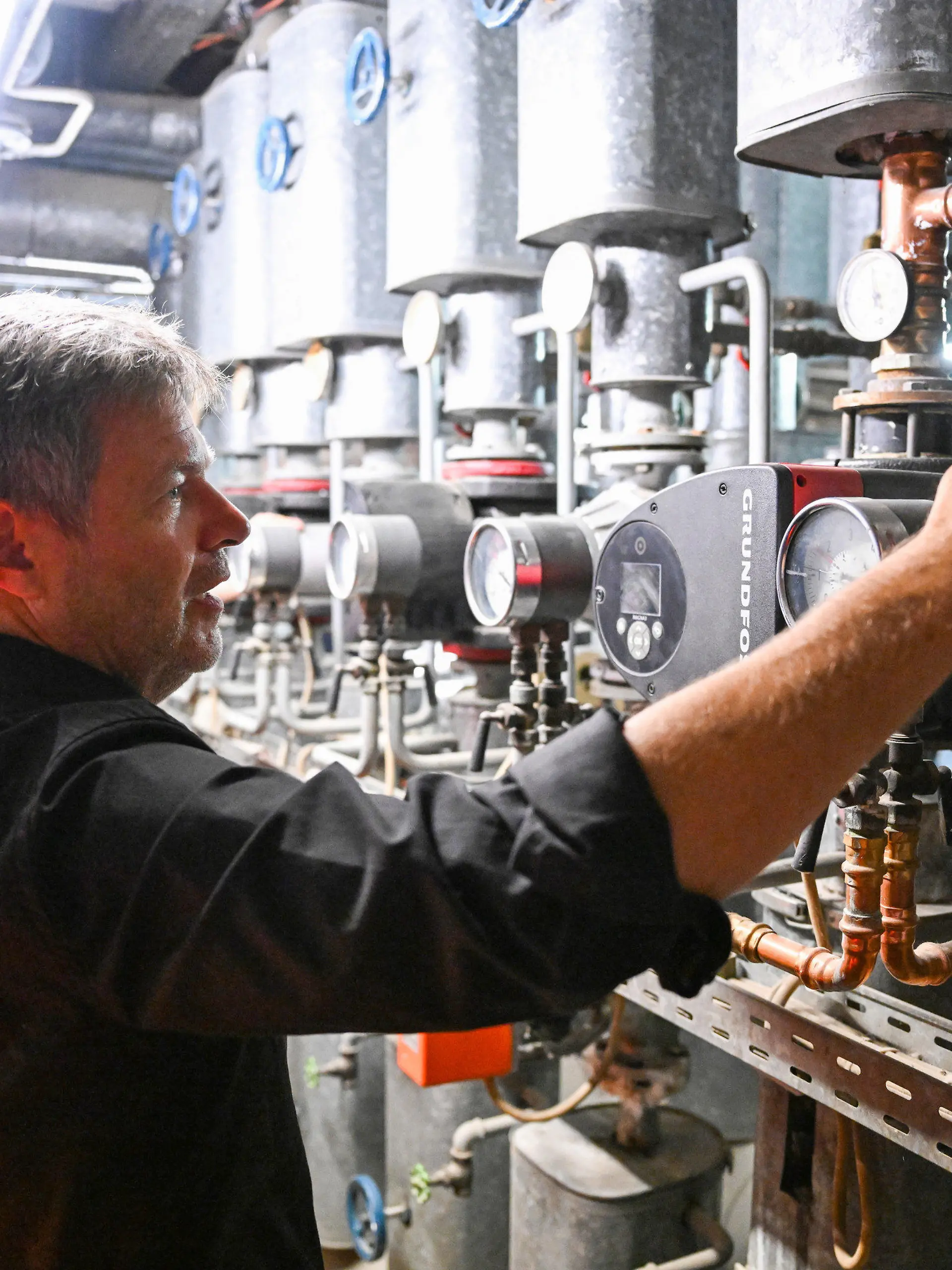 11.07.2023, Nordrhein-Westfalen, Köln: Robert Habeck (r, Bündnis 90/Die Grünen), Bundesminister für Wirtschaft und Klimaschutz, läßt sich auf seiner Sommerreise in dem Handwerksbetrieb Temperaturwerk für Heiztechnik von dem Geschäftsführer Marco Goetzke (l) in einem Heizungskeller moderne Heiztechnik erklären. Foto: Bernd Weißbrod/dpa +++ dpa-Bildfunk +++