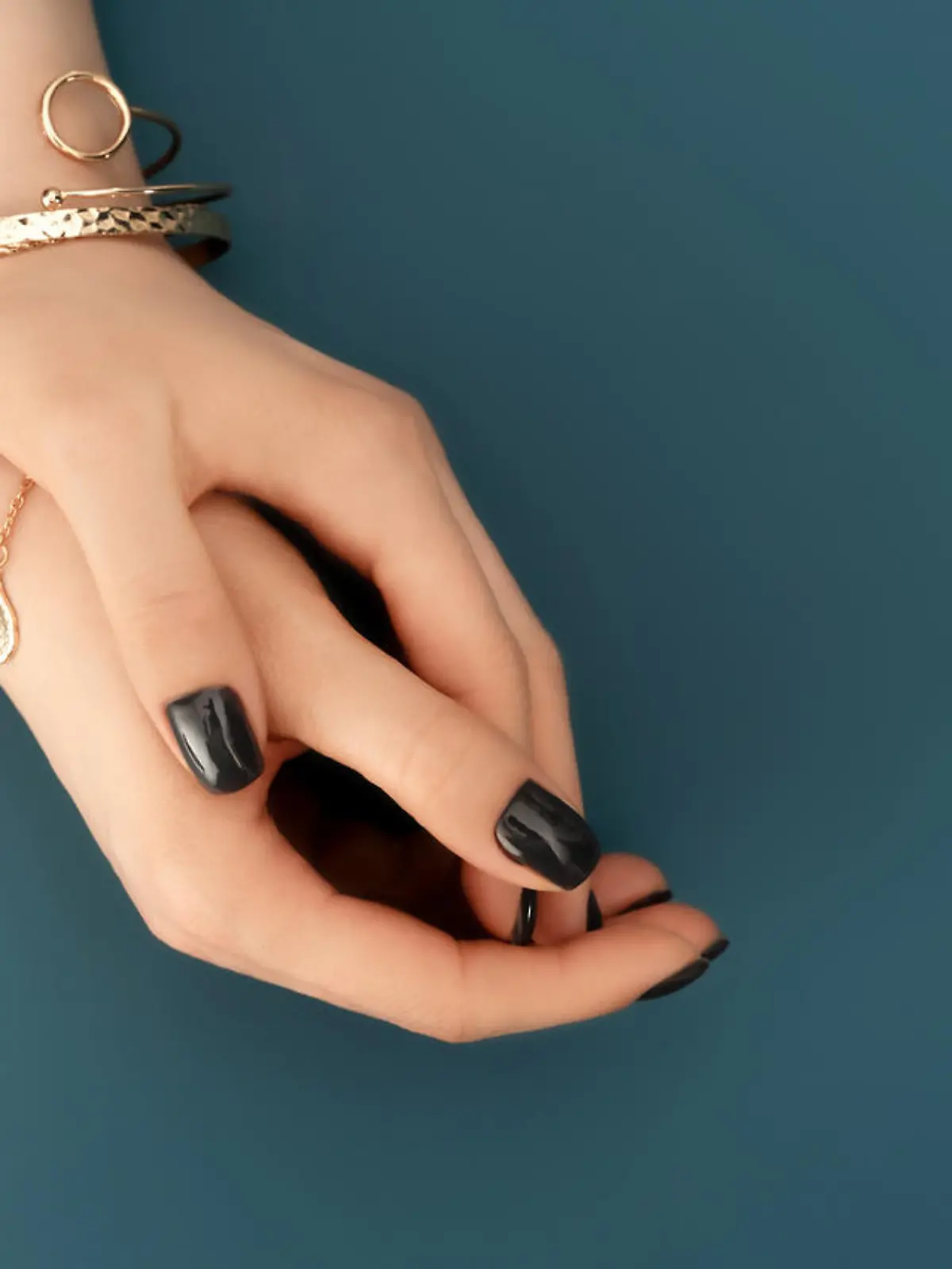 Female hands with trendy dark nail design with gold bracelets on aqua background. Luxury concept. Festive backdrop for your design. Top view.