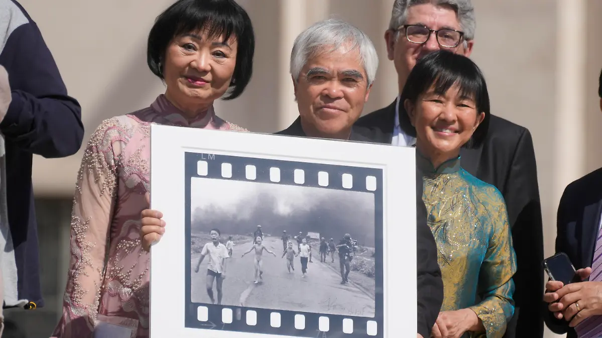 ARCHIV - 11.05.2022, Vatikan, Vatikanstadt: Der vietnamesisch-amerikanische Fotograf Nick Ut (M), hält sein mit dem Pulitzer-Preis ausgezeichnetes Foto «Napalm Girl», flankiert von Phan Thi Kim Phuc (l), die auf diesem Foto abgebildet ist, während sie auf ein Treffen mit dem Papst warten. Es ist eine der denkwürdigsten Aufnahmen des 20. Jahrhunderts: Nick Ut drückt auf den Auslöser, als ein vietnamesisches Dorf mit Napalm angegriffen wird. Warum bewegt das Foto der Neunjährigen bis heute? (zu dpa "Ikone der Fotografie und des Friedens: 50 Jahre «Napalm-Mädchen») Foto: Gregorio Borgia/AP/dpa +++ dpa-Bildfunk +++