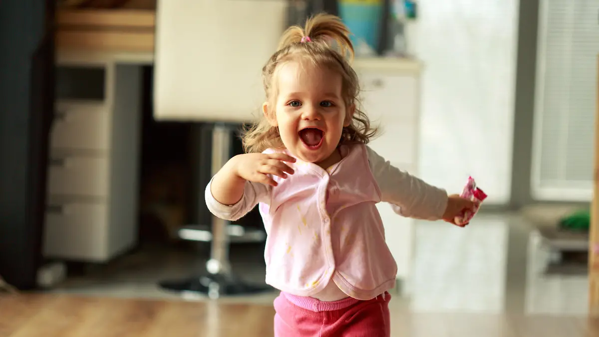 Three quarter length shot of jolly little baby girl running towards someone behind a camera and smiling with excitement.