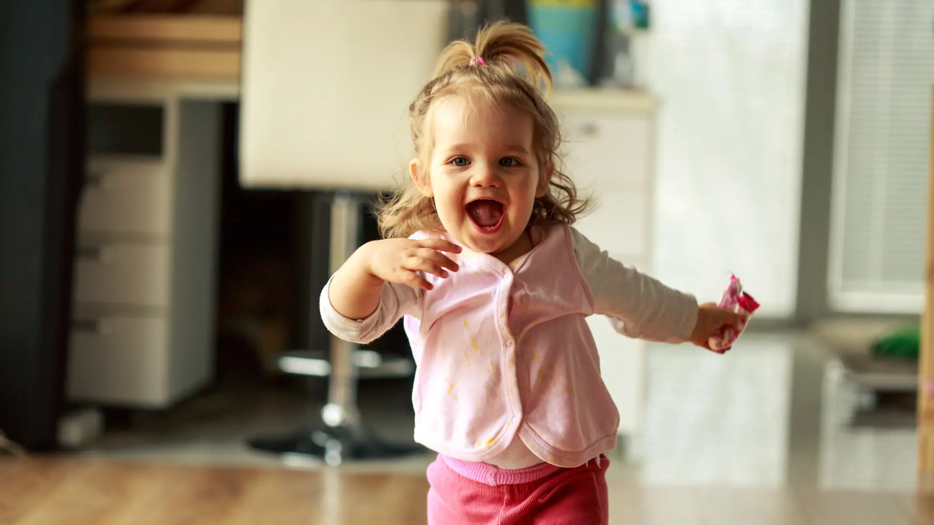 Three quarter length shot of jolly little baby girl running towards someone behind a camera and smiling with excitement.