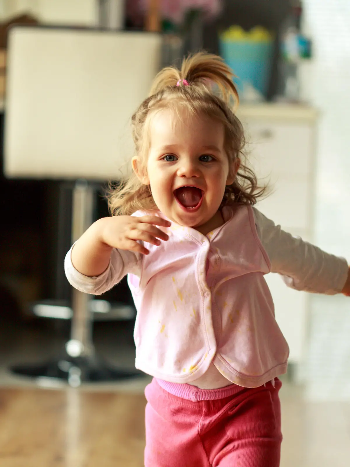 Three quarter length shot of jolly little baby girl running towards someone behind a camera and smiling with excitement.