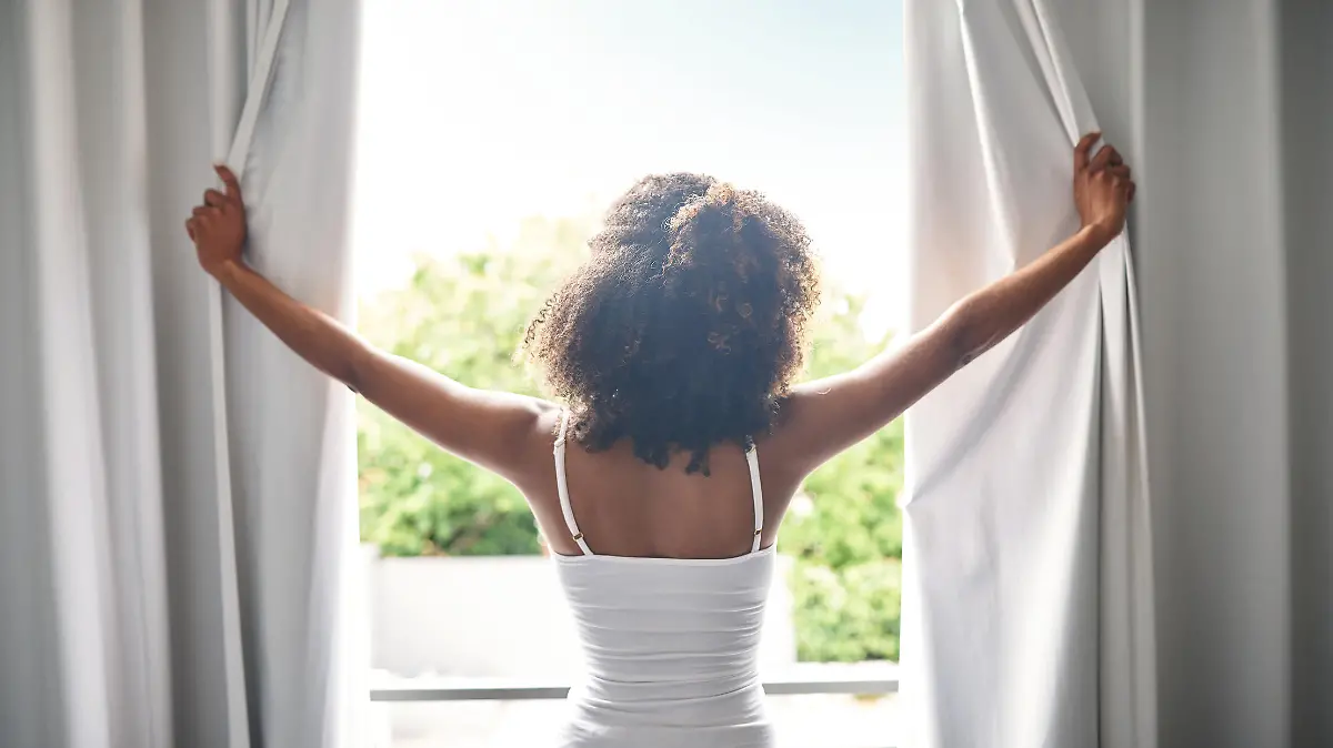Rearview of a young woman opening the curtains in her bedroom