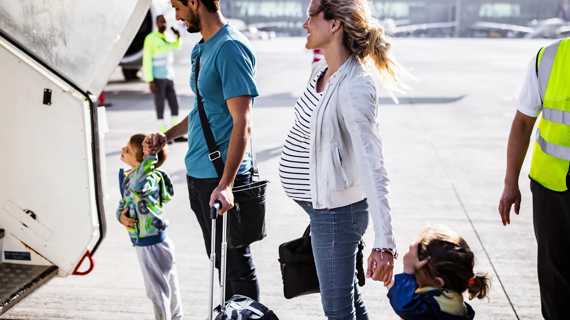 Young happy family holding hands while about to board into an airplane. Focus is on woman.