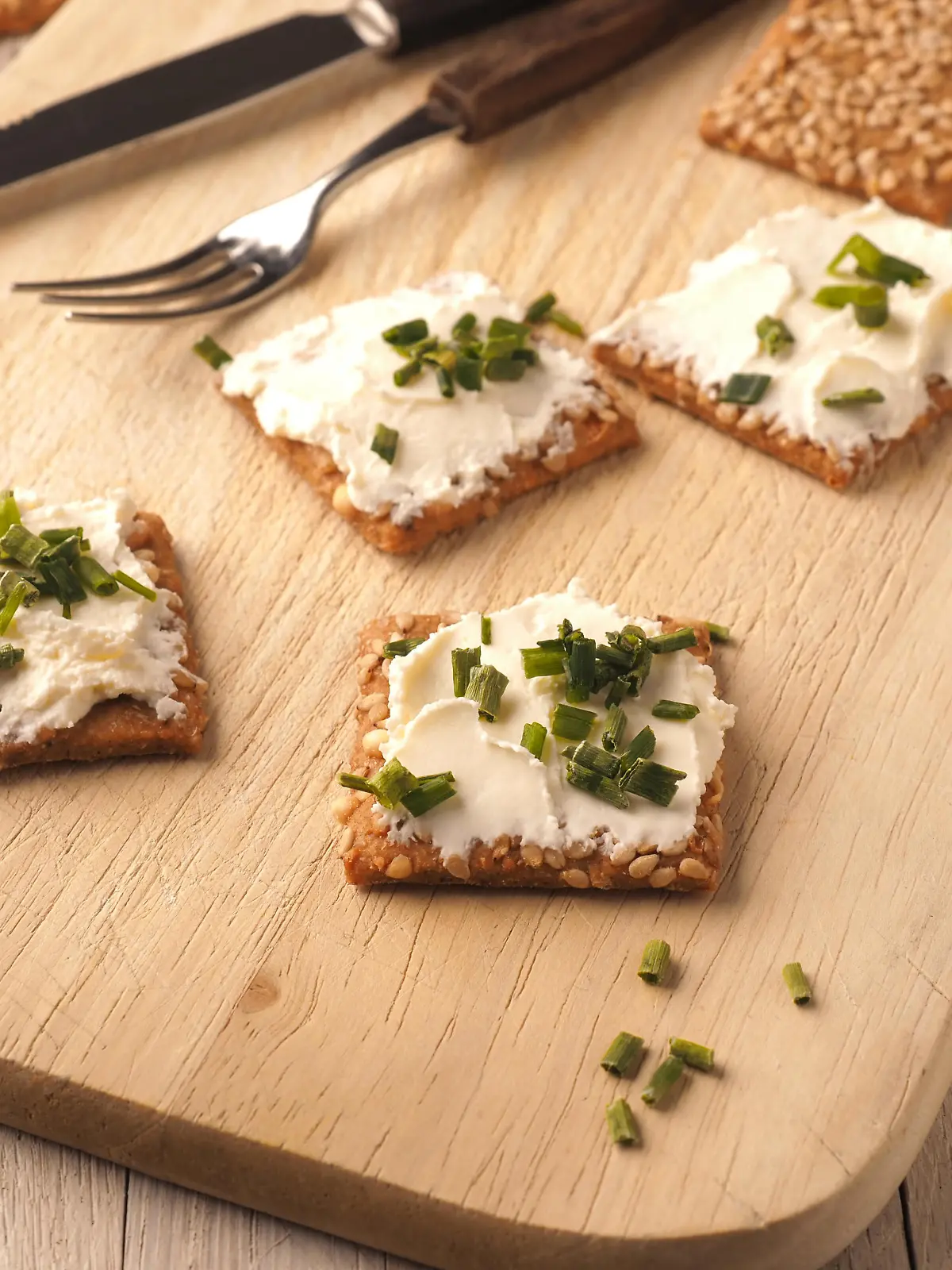 Sesame crackers with cream cheese and chives on a wooden board, healthy food concept