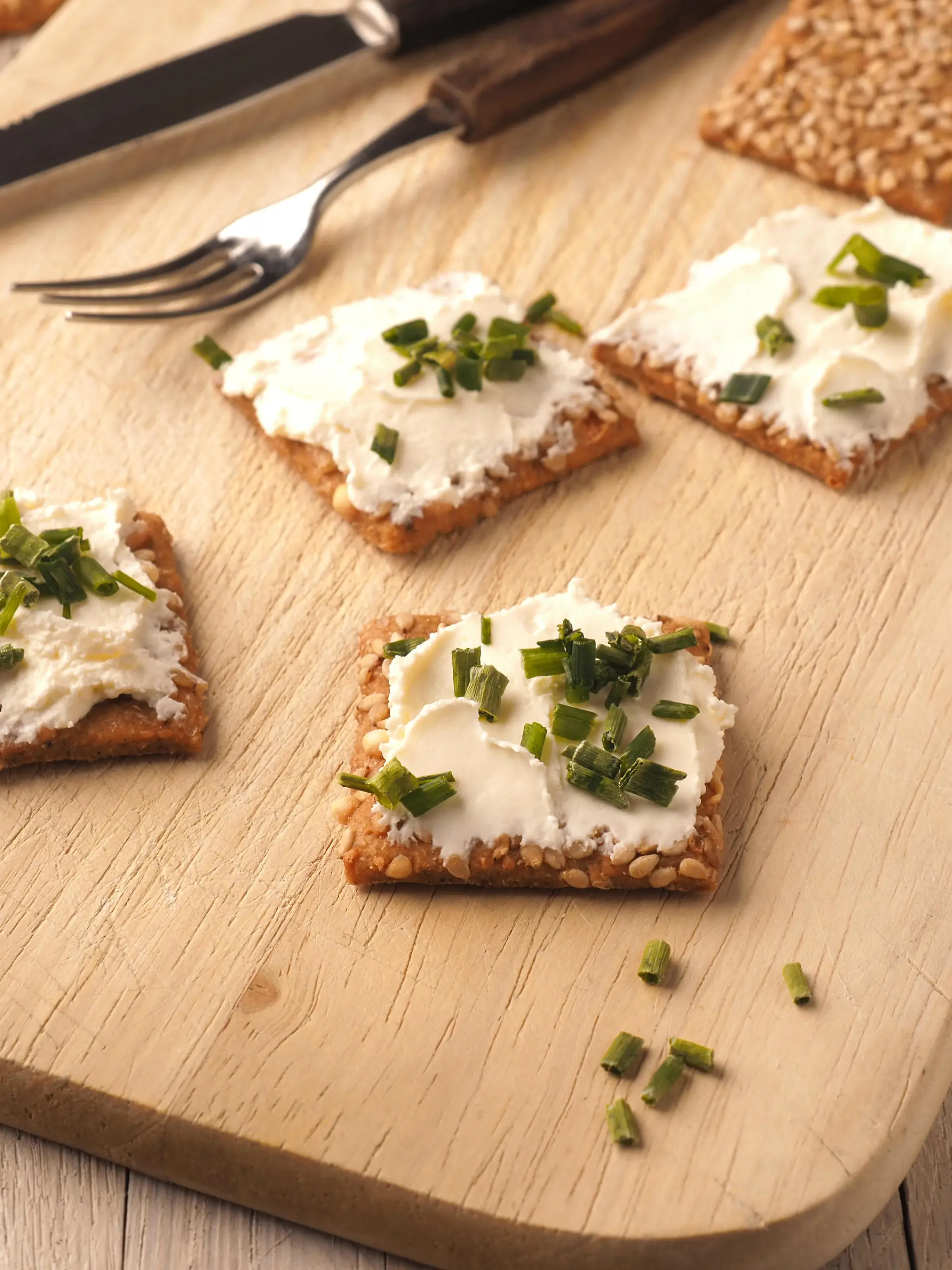Sesame crackers with cream cheese and chives on a wooden board, healthy food concept