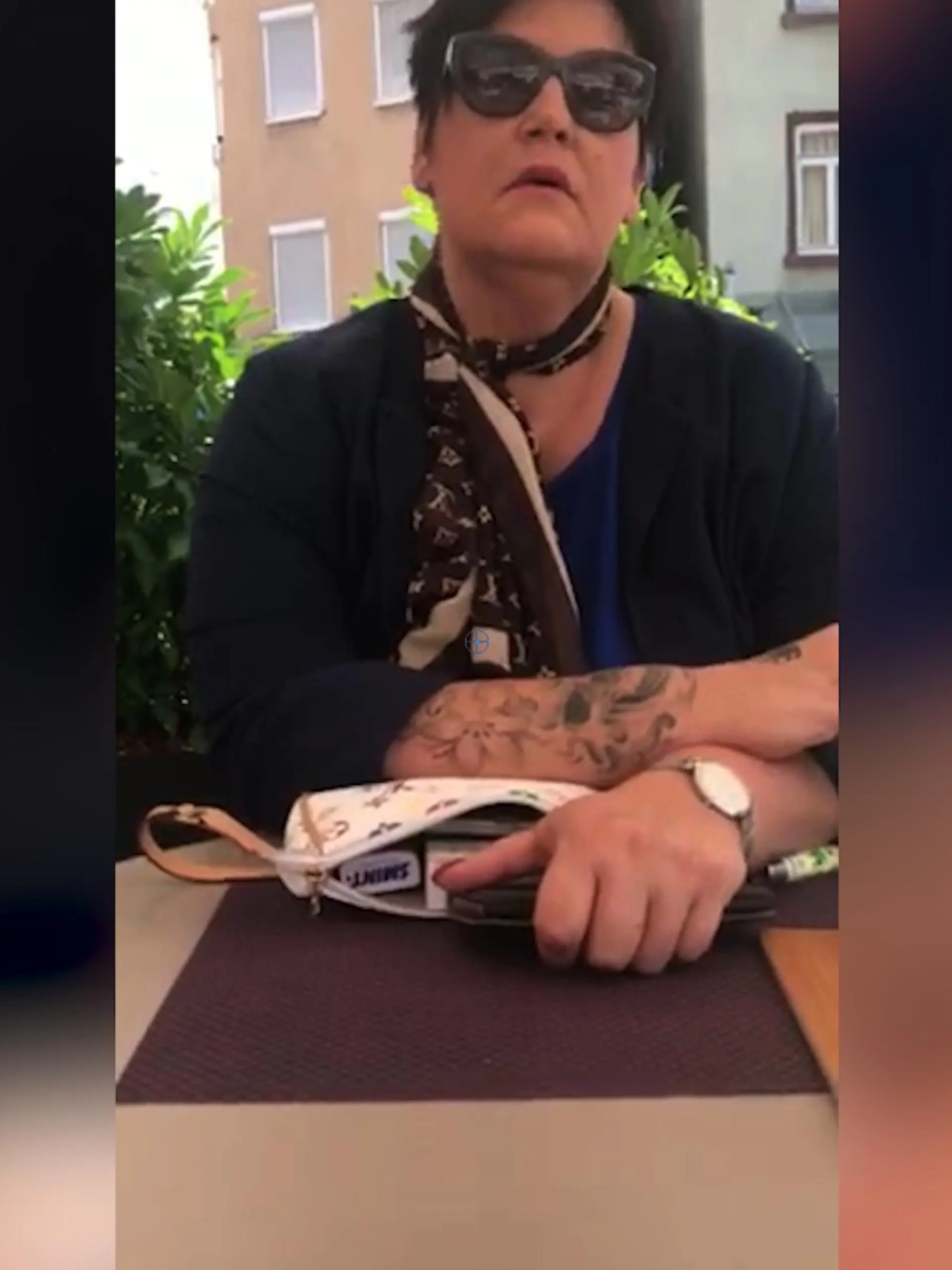 Eine Frau sitzt in einem Café auf der Terrasse und raucht.