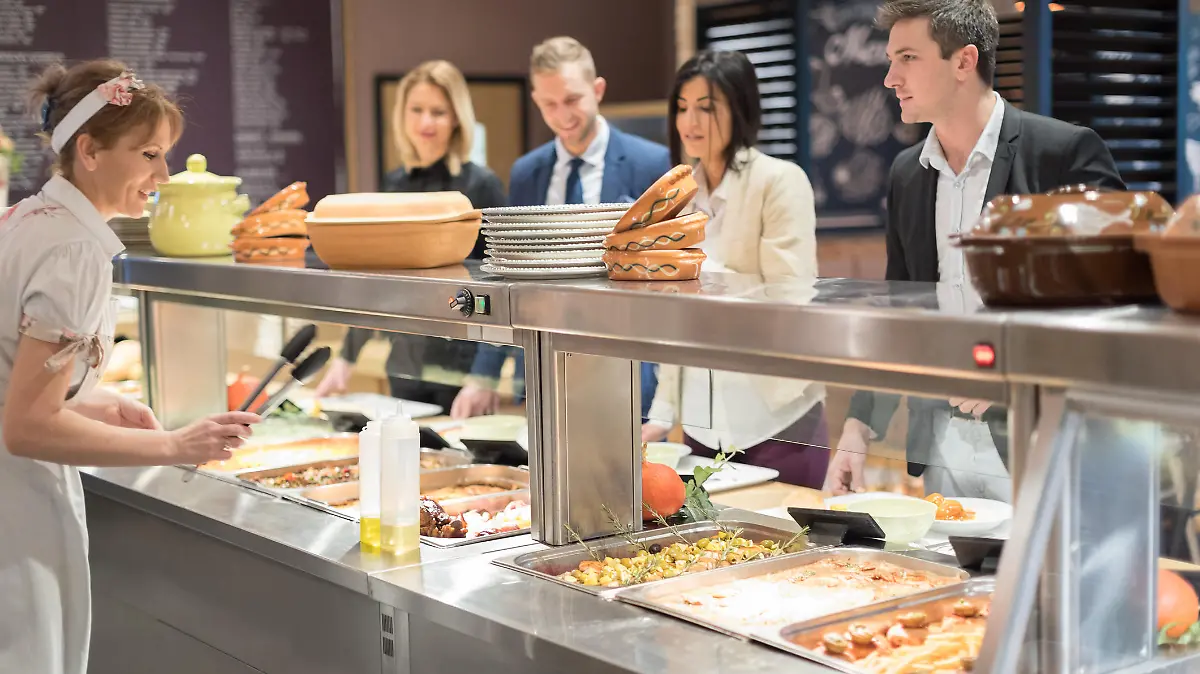 Cafeteria worker serving lunch, people waiting in line