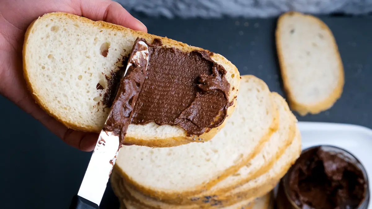 Sweet chocolate cream in jar on table. Nutella with buttered bread