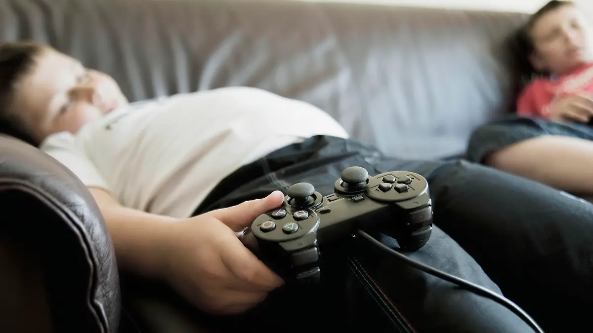 Two boys sleeping on sofa while holding games consoles