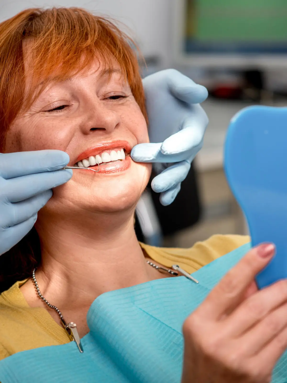 Smiling senior woman with new dental implants sitting in the dental office and looking at the mirror