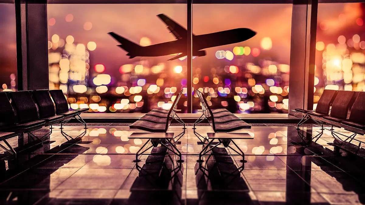 Empty airport lounge shot at night in front of the city skyline with airplane taking off against the bright lit of the city.